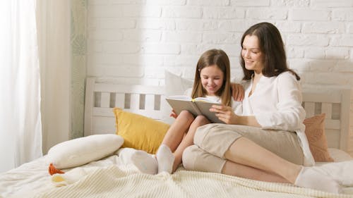 A Woman and a Girl Reading Book on Bed