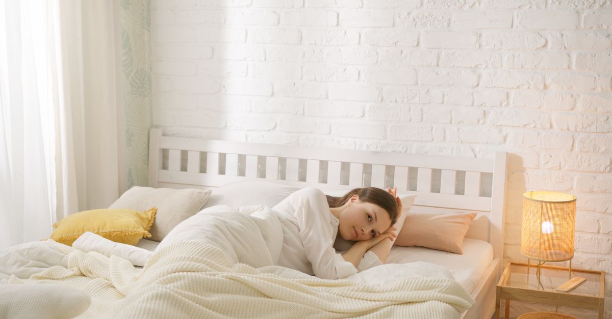 A woman relaxing in a cozy bed during the morning in a minimalist bedroom with soft lighting.