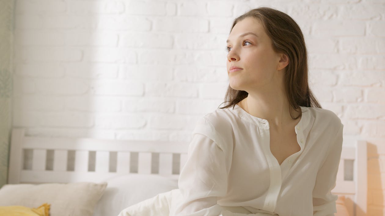 Free Woman in White Long Sleeve Shirt Sitting on White Bed Stock Photo