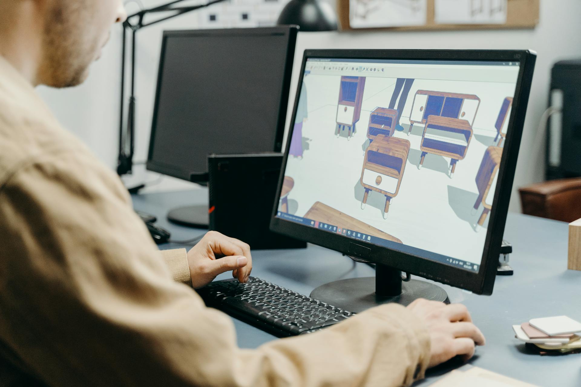 A product designer using a computer for 3D furniture modeling in an office setting.