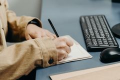 Close-up of hands writing in a notebook on an office desk with keyboard.