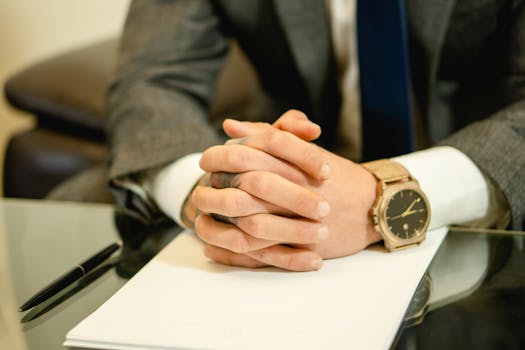 Close-up of a businessman in a suit with hands folded on a desk, wearing a wristwatch.