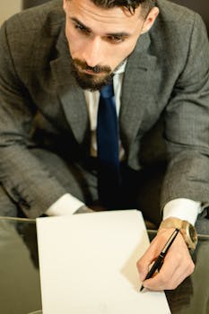 Caucasian man in deep thought writing on paper, dressed in a suit.
