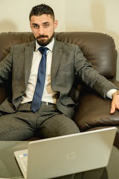 Confident business professional in gray suit with laptop in an office setting.