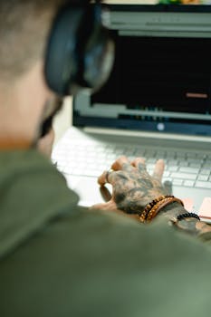Close-up of tattooed hand typing on laptop, highlighting modern work environment.