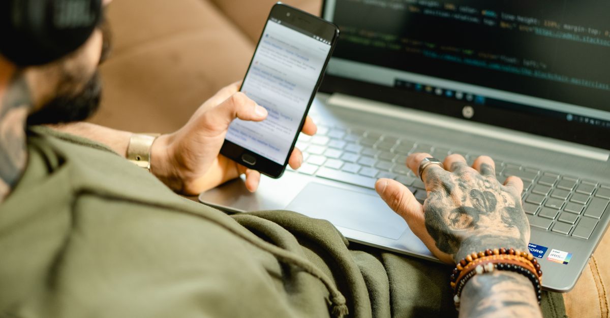 Gen Z developer typing code while watching tutorial on smartphone, split screen with AI chatbot open