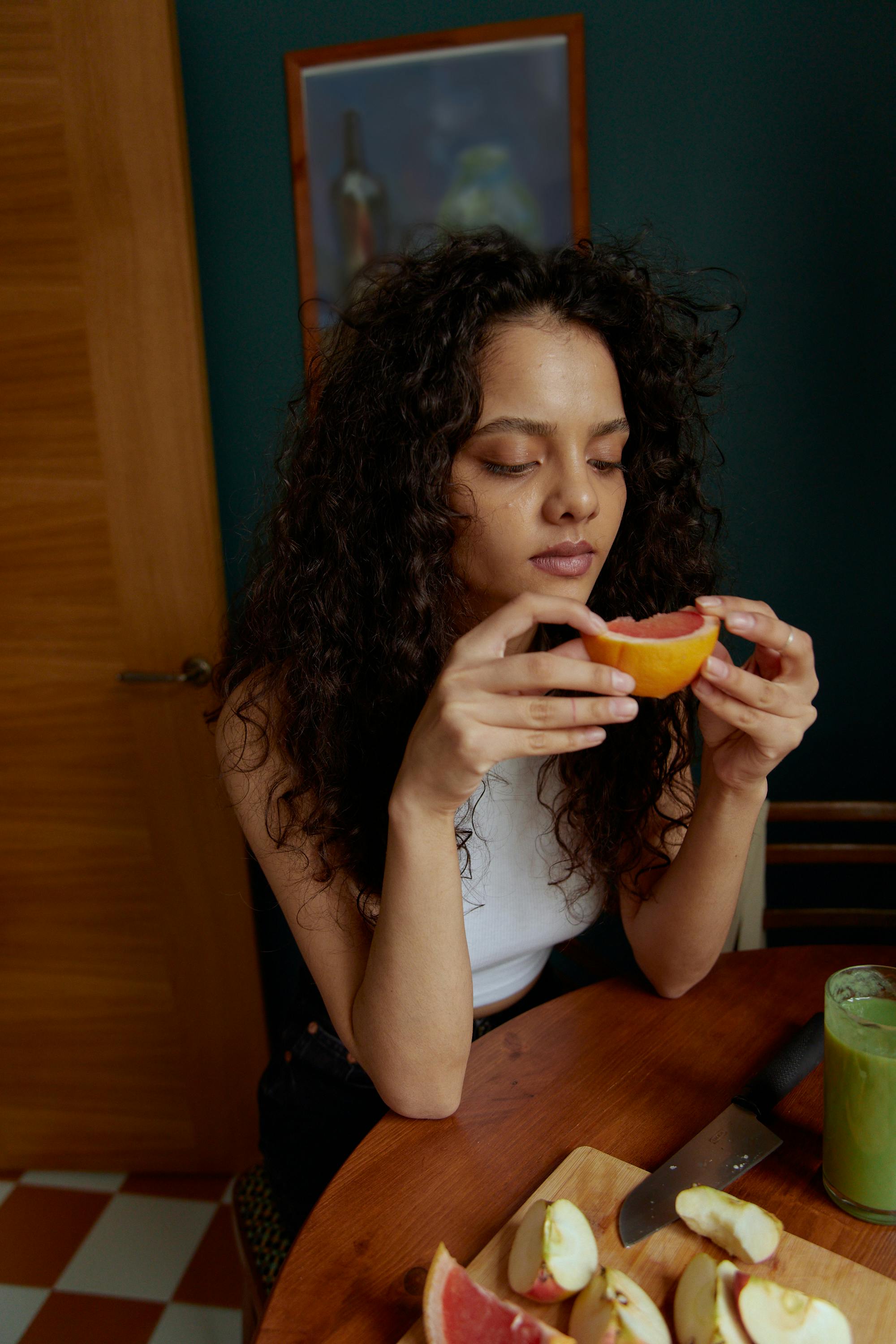 Woman in White Tank Top Eating Orange Fruit
