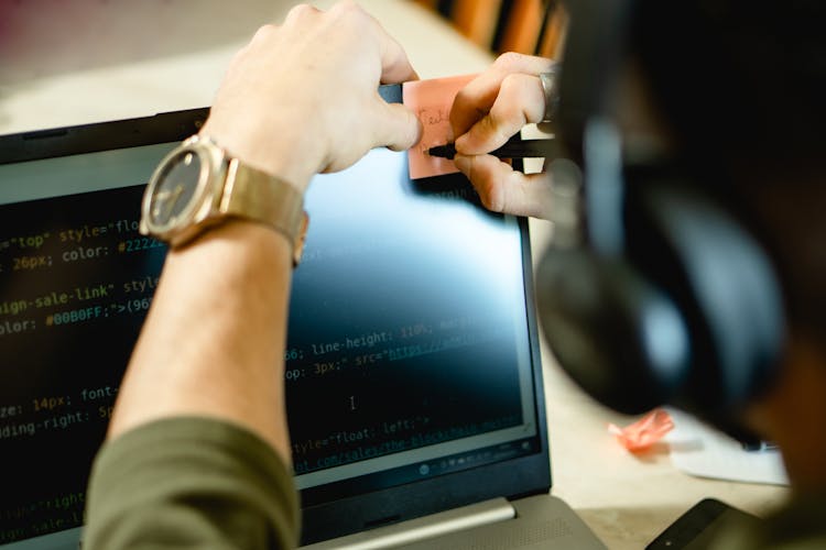 A Person Writing On The Sticky Note On The Computer Screen