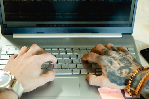 Close-up of tattooed hands typing on a laptop keyboard, focusing on productivity and creative work.