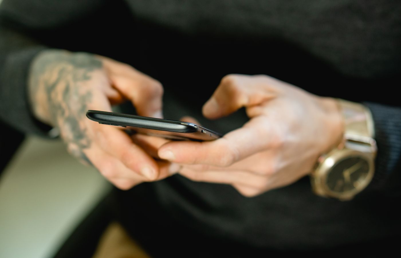 Tattooed hands holding a smartphone, showcasing digital connectivity.