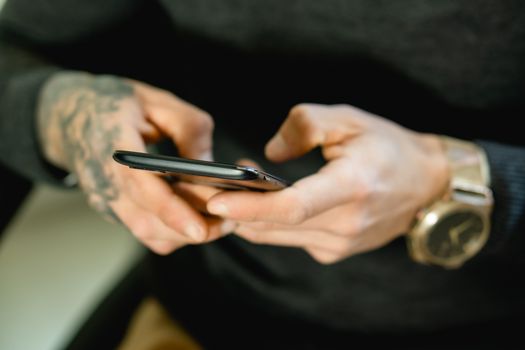 Tattooed hands holding a smartphone, showcasing digital connectivity.