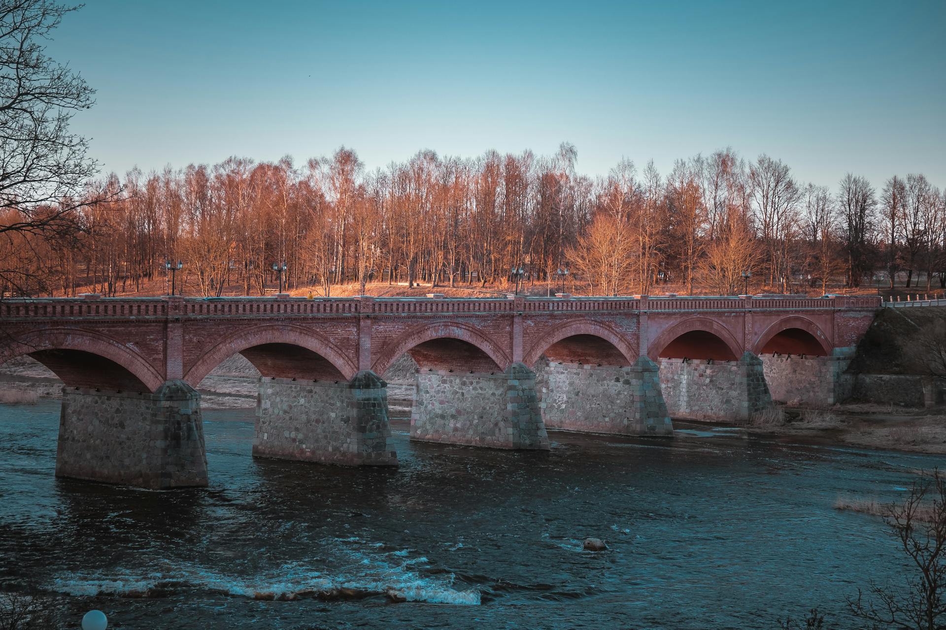 Medieval brick bridge spanning Venta River, Kuldīga, Latvia during autumn.