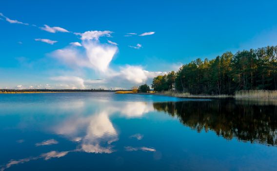 Calm lake reflecting vibrant sky and lush trees in Riga, Latvia.