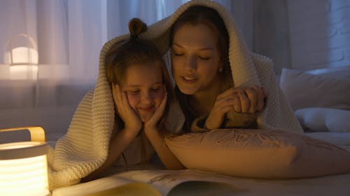 Free Mother and Daughter Lying on Bed while Reading a Book Stock Photo