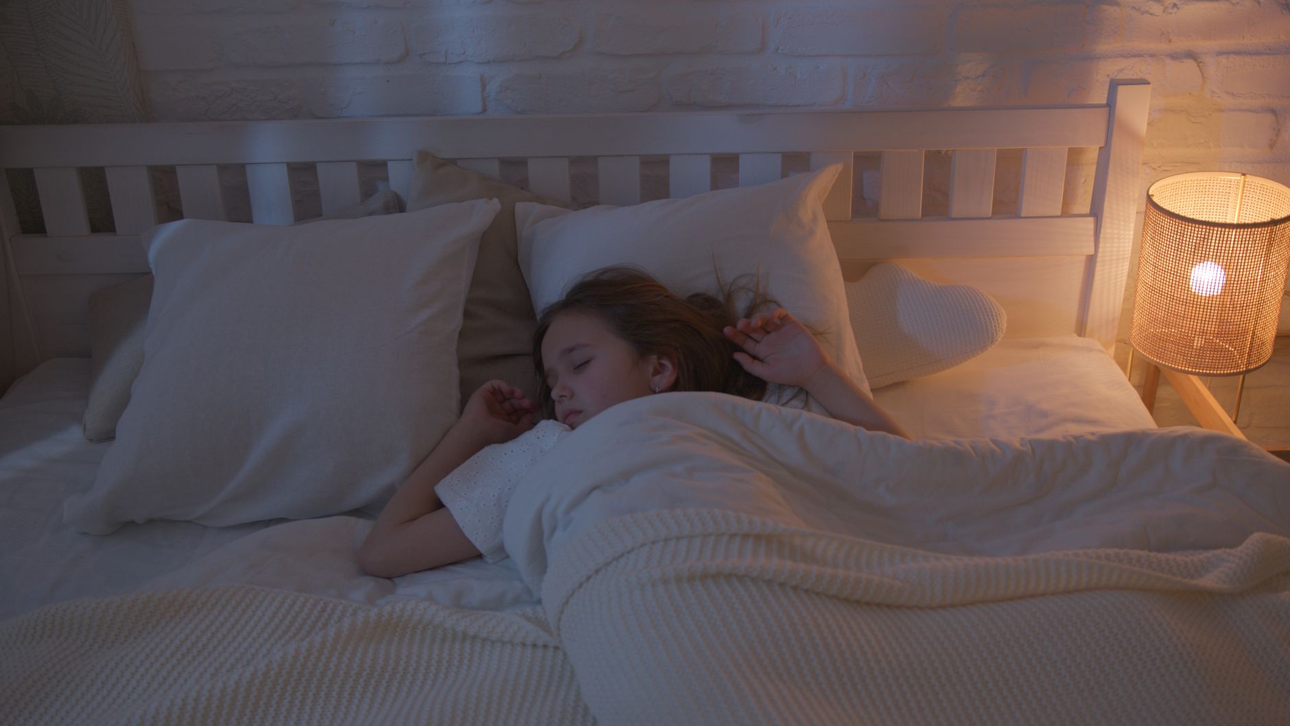 A young girl peacefully sleeping in a cozy, dimly lit bedroom with a night lamp.