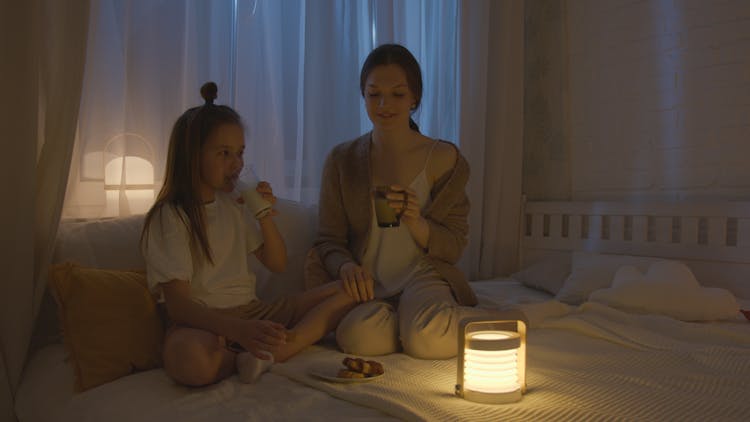 A Kid Drinking A Glass Of Milk Beside Her Mother