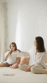 A mother and daughter sharing a tender moment while sitting on a bed in a bright room.