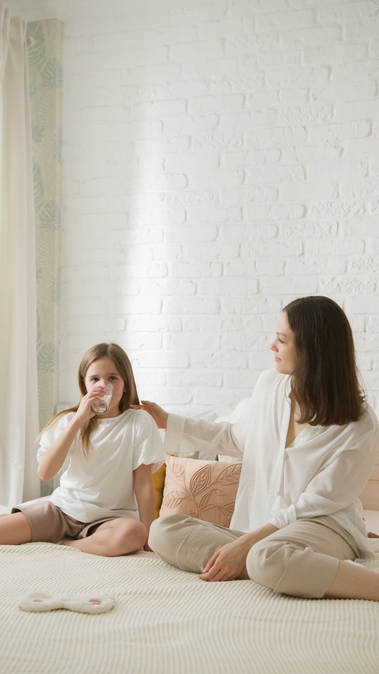 A Daughter Drinking A Glass Of Milk Beside Her Mother