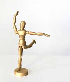 A golden wooden mannequin striking a ballet pose against a white background.