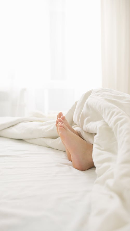 Free A Person Feet on Bed Covered With White Blanket Stock Photo