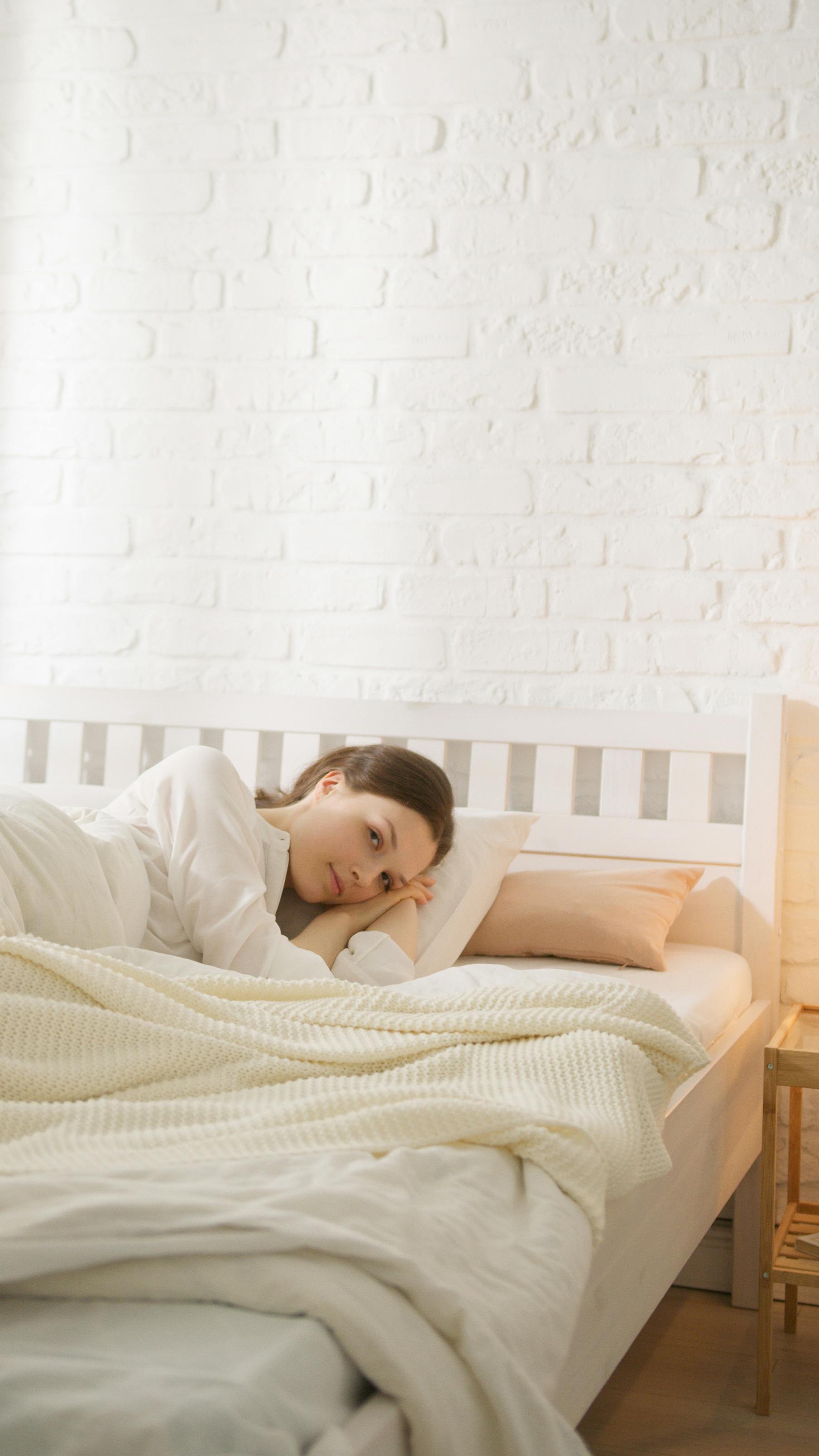 Free Woman lying comfortably in a cozy bedroom with warm bedding and soft light. Stock Photo