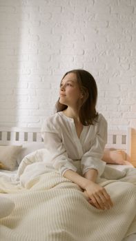 Young woman sitting comfortably on bed, enjoying a peaceful morning at home.