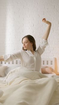 Woman enjoying a relaxed morning, stretching comfortably in bed with soft lighting.
