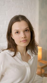 A serene portrait of a woman in a white shirt, softly lit indoors, conveying calm and elegance.