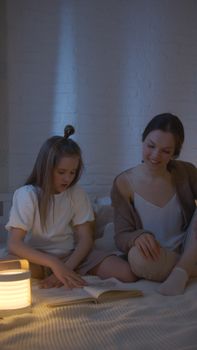 A mother and her daughter enjoy nighttime reading, fostering togetherness and bonding.