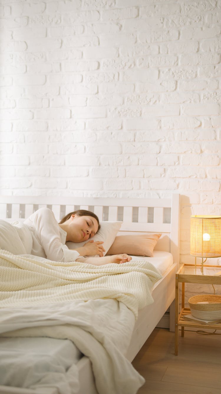 A Woman Sleeping On Her Bed Beside A Lamp