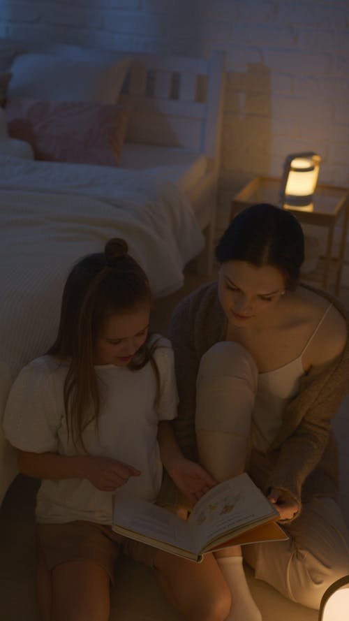 Mother and Daughter Reading a Book while Sitting on the Floor