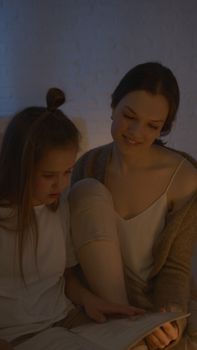 A mother and daughter share a cozy reading moment together in a warm, dimly lit room.