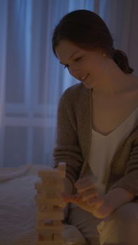 A woman enjoying a relaxing game of Jenga indoors during the evening hours.