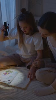 A mother and daughter enjoy nighttime reading with a flashlight, fostering bonding and learning.