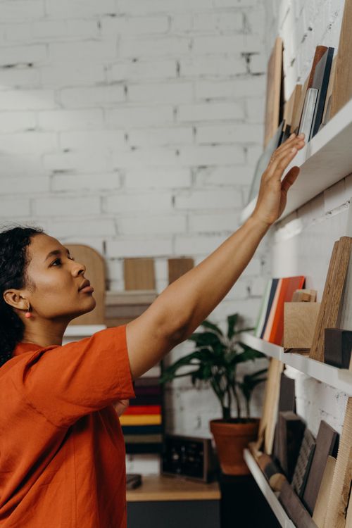 Free A woman in an orange top reaches for a book on a shelf in a modern indoor space. Stock Photo