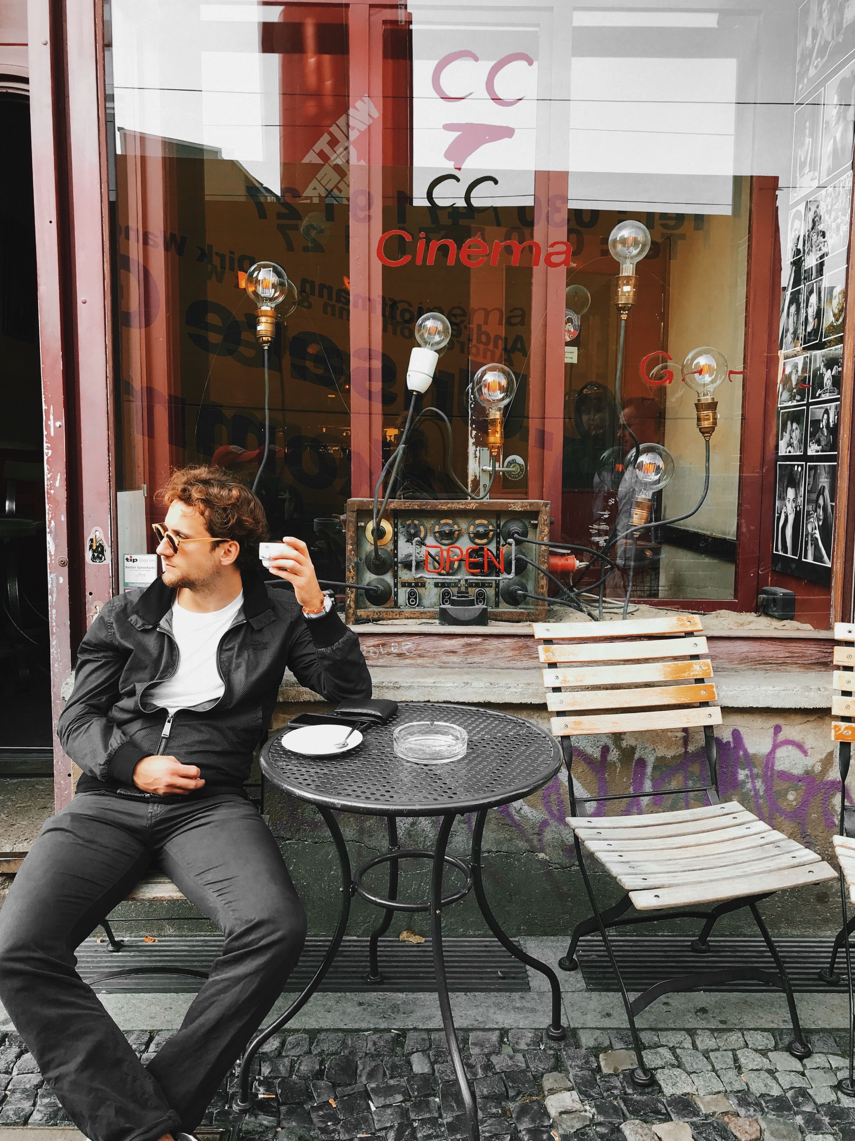 Man casually sitting outside a cafe in Berlin, enjoying a drink on a stylish urban street.