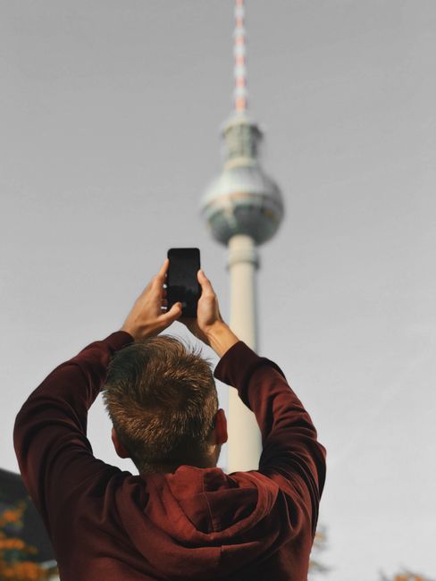 Man photographing Berlin's iconic TV Tower with smartphone. Captures modern travel vibe.
