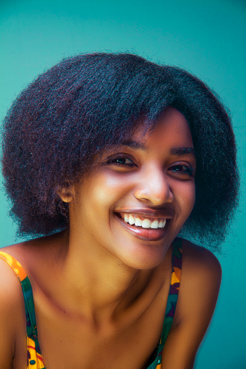 Free Portrait of a smiling woman with afro hair and colorful attire against a vibrant background. Stock Photo