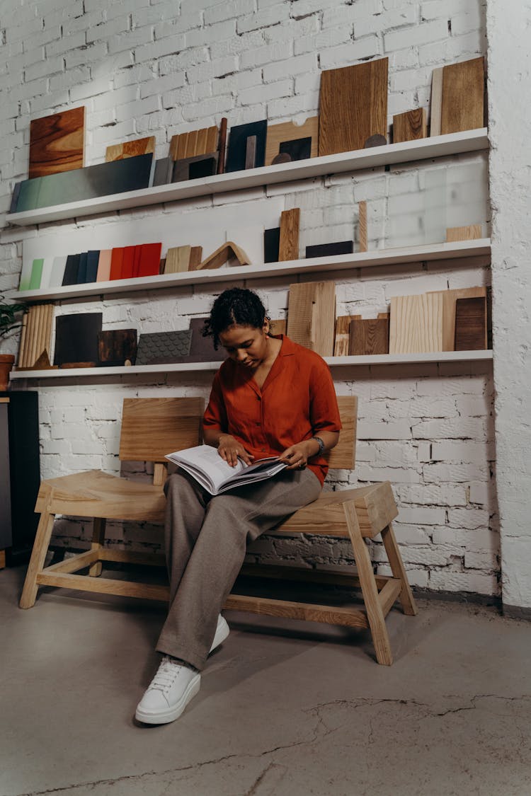 Woman Looking At A Catalog While Sitting On A Wooden Bench