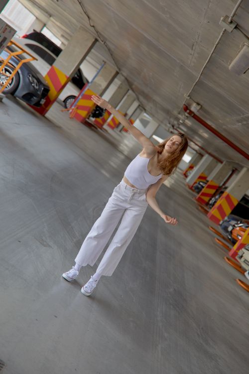 Free A fashionable woman dances expressively in a modern parking garage with a unique tilt angle. Stock Photo