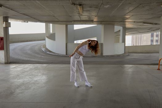 Fashion model striking a pose in a stylish white outfit in a modern parking garage.