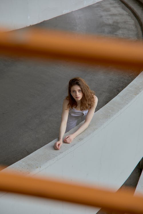 Woman in White Tank Top Stretching Arm on Concrete Barrier