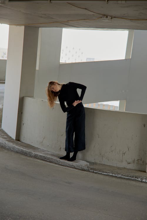 Woman in Black Clothing Bending Near Concrete Barrier