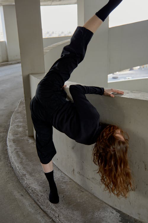 Woman in Black Clothing Stretching Leg Near Concrete Barrier