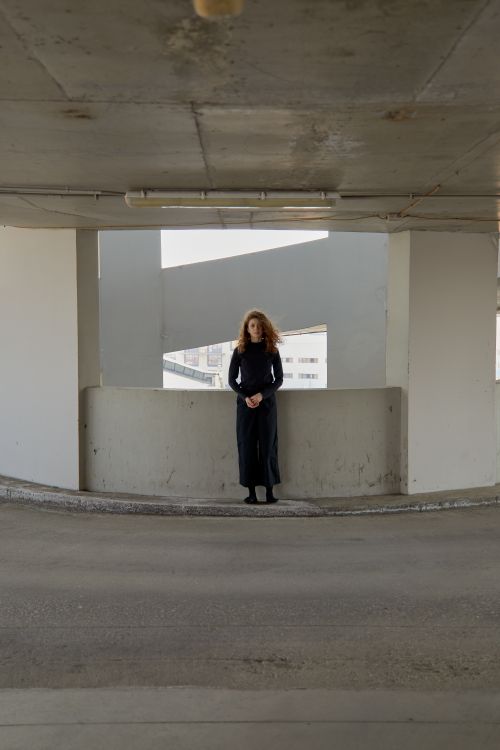 Free A woman in a black dress stands alone in an urban concrete setting, evoking solitude. Stock Photo