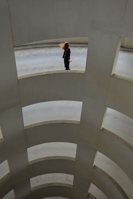 A woman stands on a curved path in a modern concrete spiral structure.