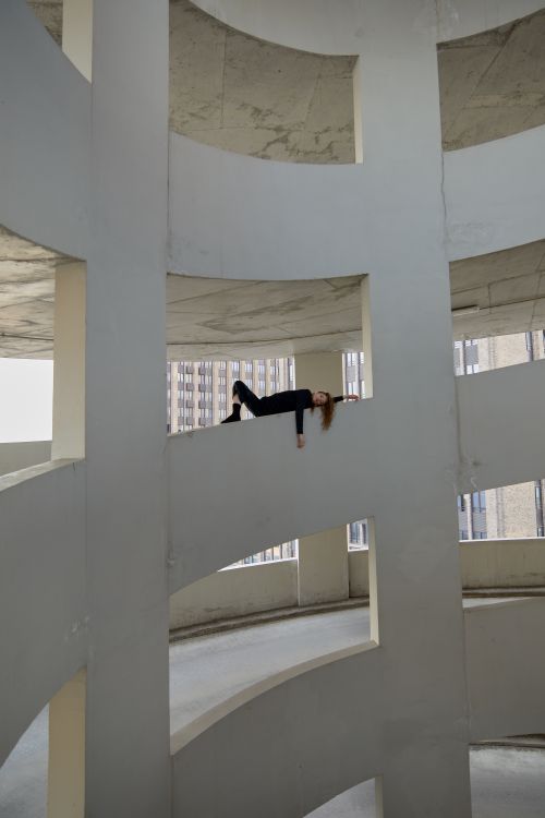 Free Woman in a unique dance pose on curved structure of urban parking garage, showcasing modern architecture. Stock Photo