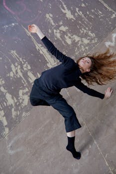 Woman dancer in black performing a striking contemporary dance move on a textured concrete floor.
