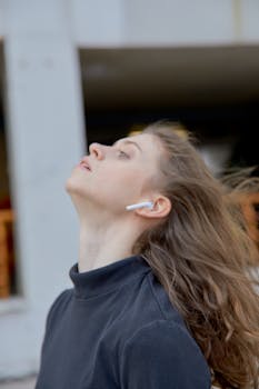 Portrait of a young woman wearing wireless earbuds, looking up with wind in her hair on a breezy day.