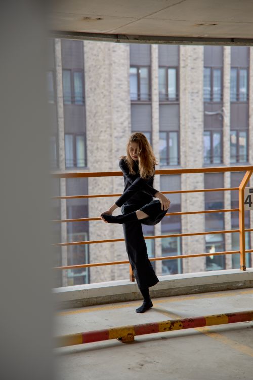 Free Caucasian woman dancer balancing in a parking lot with city buildings in the background. Stock Photo